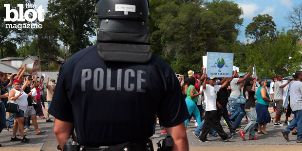 The DOJ criticized Ferguson police for racially profiling citizens for several years. It also released a 105-page report on the death of Michael Brown. In this photo from Aug. 11, a police officer in riot gear watches protesters march two days after Brown was shot by Officer Darren Wilson. (© Robert Cohen/ZUMA Press/Corbis photo)